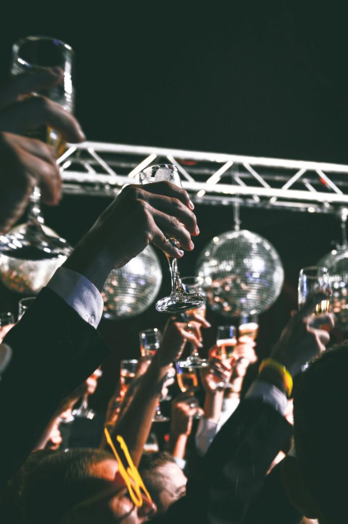 A festive gathering with people raising glasses in a toast under shiny disco balls at a night event.