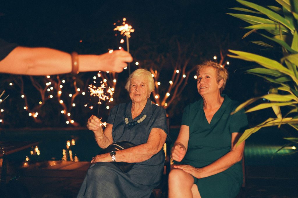 Two women watch a sparkler at night.